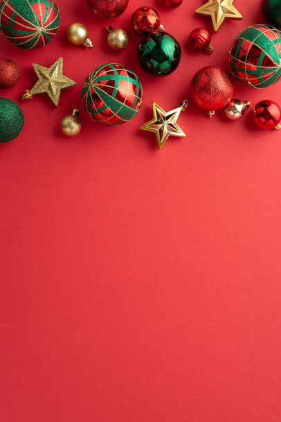 Karácsonyfa dekoráció koncepció. Felülnézet függőleges fotó csillag díszek arany zöld és piros baubles elszigetelt piros háttér copyspace - Fotó, kép