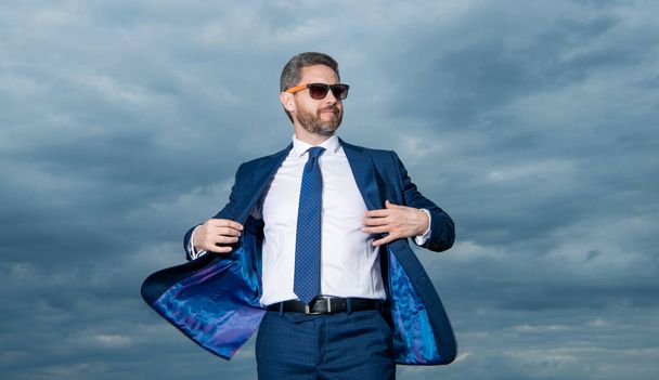 Businessman wearing open suit jacket fluttering in wind. Grizzled businessman in sunglasses. Businessman sky background. - Photo, Image
