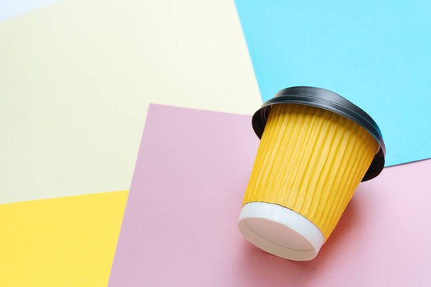 Sarı kahve fincanı tasarımcının masasındaki renkli kağıtta yaratıcı bir karmaşanın içinde yatıyor. Mavi, turuncu ve pembe arka plan. Metin için Boşluğu Kopyala - Fotoğraf, Görsel
