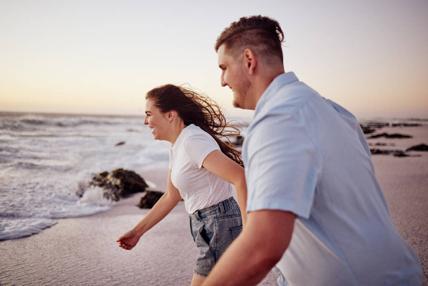 Αγάπη, παραλία και το ζευγάρι κρατώντας τα χέρια τρέχει στο νερό σε ένα ρομαντικό βράδυ ηλιοβασίλεμα μαζί σε εξωτερικούς χώρους στη φύση. Χαμόγελο, ρομαντισμό και ευτυχισμένη γυναίκα σε διακοπές μήνα του μέλιτος με έναν ενθουσιασμένο σύντροφο στη θάλασσα. - Φωτογραφία, εικόνα