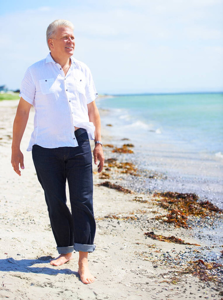 Taking in the beauty of the ocean. A senior man walking barefoot on the shoreline - 写真・画像