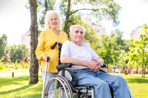 Beautiful senior couple with disability outdoors - Old people in the age of 60, 70, 80 having fun and spending time together, concepts about elderly, seniority, healthcare and wellness aging - Foto, Imagem