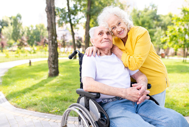 Beautiful senior couple with disability outdoors - Old people in the age of 60, 70, 80 having fun and spending time together, concepts about elderly, seniority, healthcare and wellness aging - Φωτογραφία, εικόνα