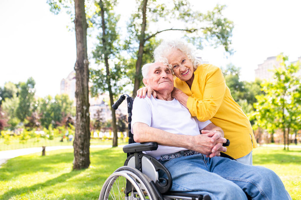 Beautiful senior couple with disability outdoors - Old people in the age of 60, 70, 80 having fun and spending time together, concepts about elderly, seniority, healthcare and wellness aging - Foto, imagen