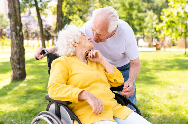 Beautiful senior couple with disability outdoors - Old people in the age of 60, 70, 80 having fun and spending time together, concepts about elderly, seniority, healthcare and wellness aging - Photo, image