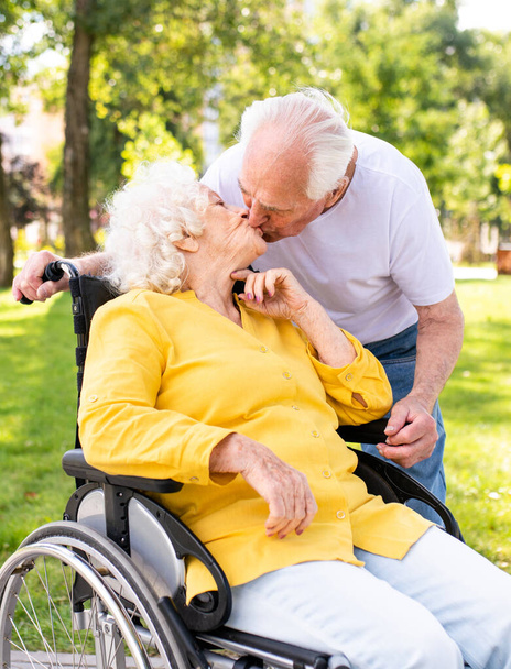 Beautiful senior couple with disability outdoors - Old people in the age of 60, 70, 80 having fun and spending time together, concepts about elderly, seniority, healthcare and wellness aging - Foto, afbeelding