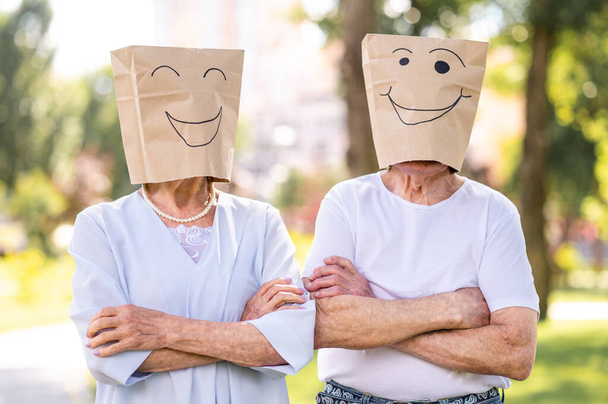 Senior couple in love with paper bags over the head romantic dating - Old people in the age of 60, 70, 80 having fun and spending time together, concepts about elderly, seniority and wellness aging - Photo, Image
