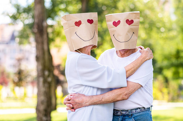 Senior couple in love with paper bags over the head romantic dating - Old people in the age of 60, 70, 80 having fun and spending time together, concepts about elderly, seniority and wellness aging - Photo, image