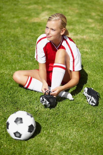 Готується до матчу. жіночий футболіст зав'язує взуття, лежачи на траві
 - Фото, зображення