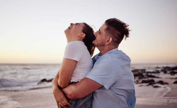 Sunset, love and young couple on the beach bonding, laughing and enjoying their honeymoon holiday. Happy, fun and man embracing and playing with woman while on romantic vacation in Miami Florida - Photo, Image