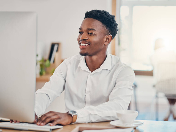 Számítógép, gépelés és fekete ember, aki az irodában dolgozik, kutatásokat végez és e-maileket ír. Technológia, munka és üzletember mosollyal az arcán a munkahelyen az innováció, internet és startup cég számára. - Fotó, kép