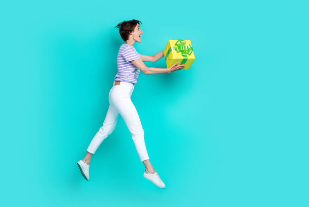 Full length photo of sweet shiny lady wear violet t-shirt giving present empty space jumping high isolated turquoise color background. - Photo, Image