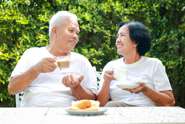 Glückliches asiatisches älteres Ehepaar sitzt morgens im Garten des Hauses und trinkt gemeinsam Kaffee. Das Konzept, dass Familie füreinander sorgt. Leben im Ruhestand - Foto, Bild