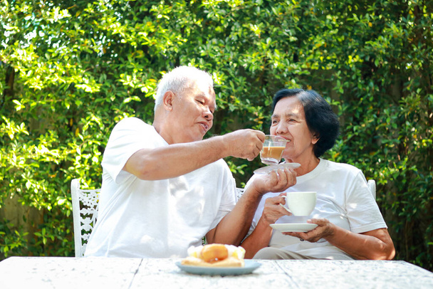 Szczęśliwa azjatycka para siedząca i pijąca kawę razem rano w ogrodzie domu. Koncepcja rodziny dbającej o siebie nawzajem. życie na emeryturze - Zdjęcie, obraz