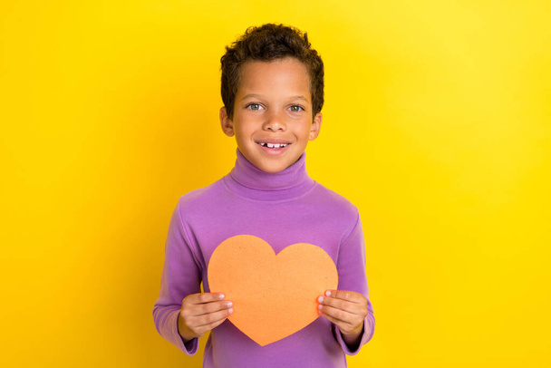 Photo of cute positive boy hands hold paper heart figure postcard isolated on yellow color background. - Foto, Imagem