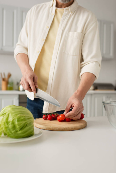 частичный вид человека в белой рубашке с ножом рядом с помидорами черри на доске - Фото, изображение
