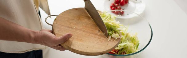 partial view of man with chopping board adding cut lettuce into bowl while preparing vegetable salad, banner - Фото, изображение