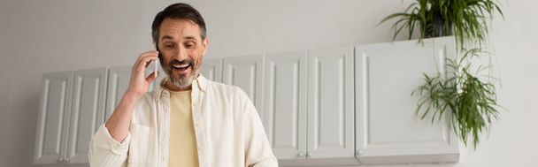 vrolijk baard man praten op mobiele telefoon in de keuken, banner - Foto, afbeelding