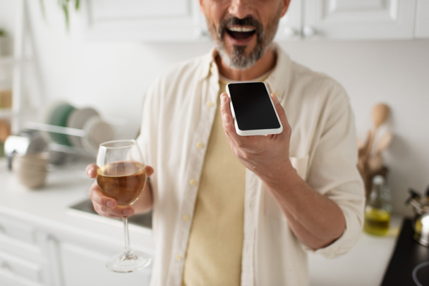 vista ritagliata dell'uomo sfocato con bicchiere di vino bianco che invia messaggi vocali sul telefono cellulare con schermo vuoto - Foto, immagini