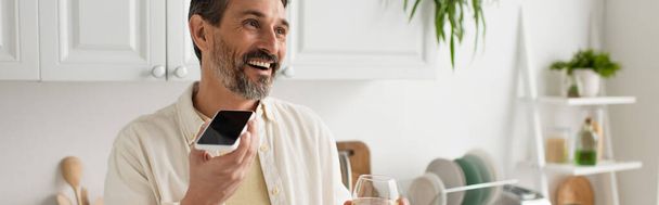 hombre alegre con copa de vino blanco enviando mensaje de voz en el teléfono inteligente con pantalla en blanco, bandera - Foto, imagen