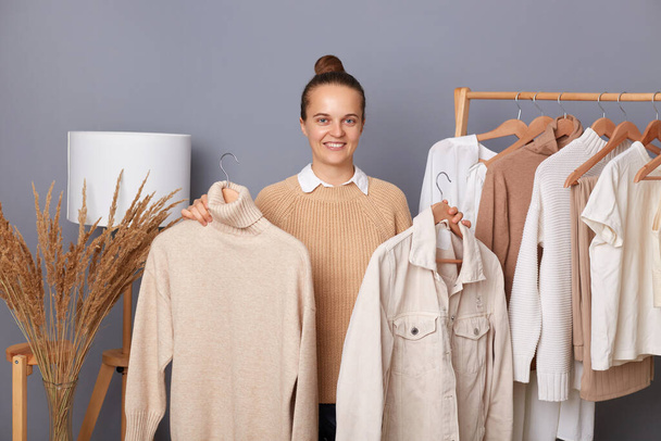 Positive beautiful woman shopper holding clothes on racks and looking at camera with happy expressing and toothy smile, choosing casual style outfit shopping in modern boutique. - Foto, afbeelding