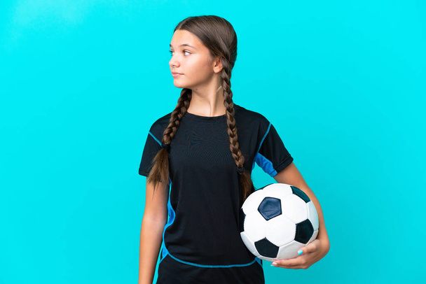Mavi arka planda, futbol topuyla izole edilmiş küçük beyaz kız. - Fotoğraf, Görsel