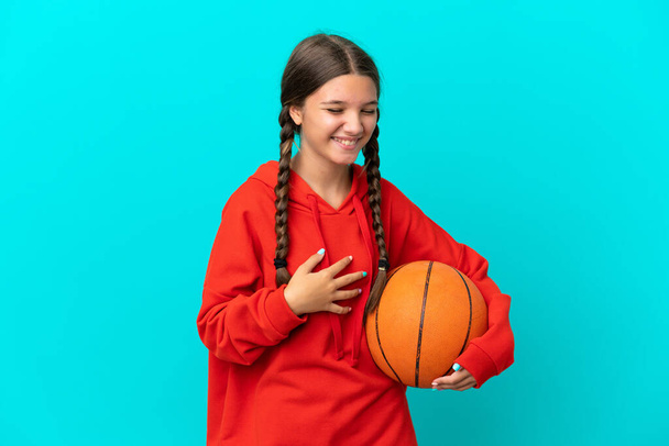 Маленькая белая девочка, играющая в баскетбол на голубом фоне, много улыбается. - Фото, изображение
