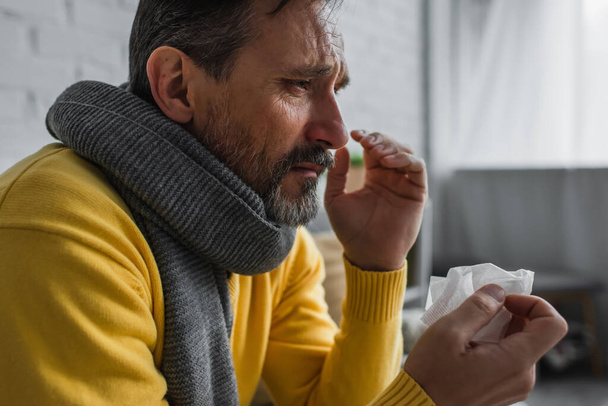 больной человек с больным горлом и насморком в теплом шарфе и с бумажной салфеткой в руках - Фото, изображение