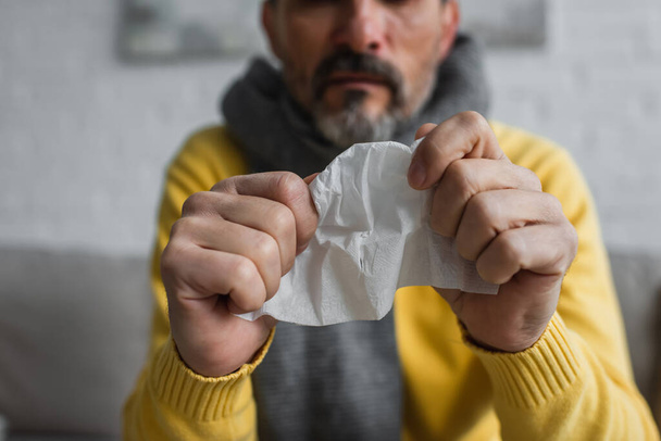 селективный фокус смятой бумажной салфетки в руках обрезанного больного человека на размытом фоне - Фото, изображение