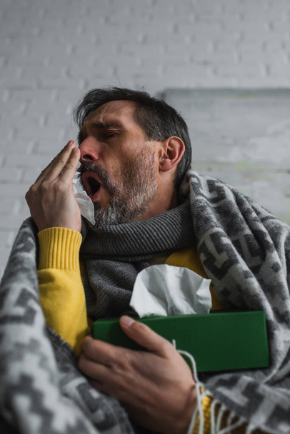 low angle view of man covering mouth with hand while coughing and holding pack of paper napkins - Photo, Image