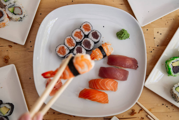 Zbliżenie młodego Azjaty jedzącego świeże sushi w japońskiej restauracji.Skup się na talerzu - Zdjęcie, obraz