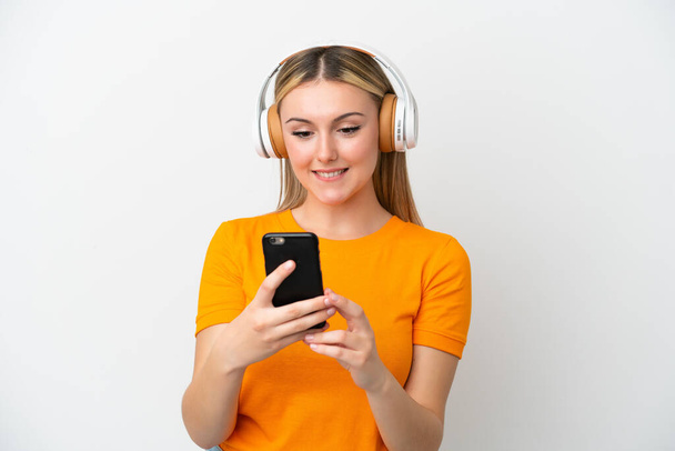 jonge Kaukasische vrouw geïsoleerd op witte achtergrond luisteren muziek met een mobiele en op zoek front - Foto, afbeelding