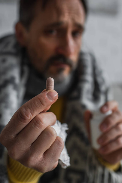 Selektiver Fokus der Pille in der Hand eines erkrankten Mannes auf verschwommenem Hintergrund - Foto, Bild