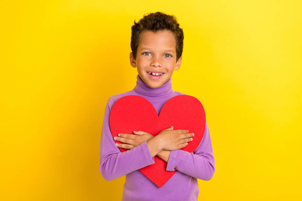 Photo of cute cheerful boy hands hold cuddle red paper heart postcard isolated on yellow color background. - Foto, Imagem