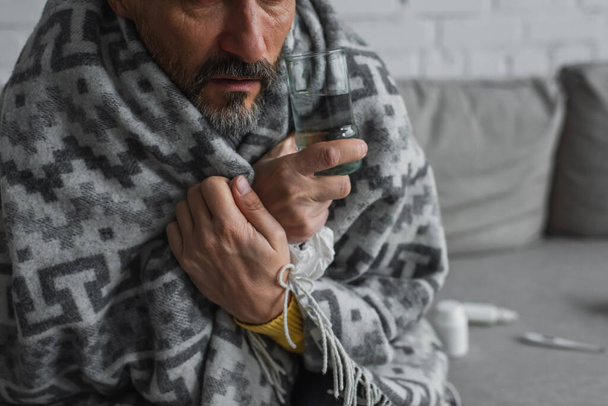 partial view of man wrapped in warm blanket holding glass of water - Fotografie, Obrázek