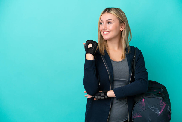 Young sport woman with sport bag isolated on blue background pointing to the side to present a product - Foto, afbeelding