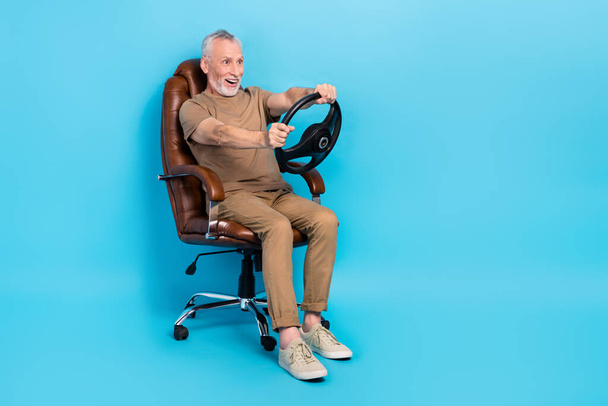 Full length photo of funky overjoyed man sit chair arms hold wheel look empty space isolated on blue color background. - Фото, зображення