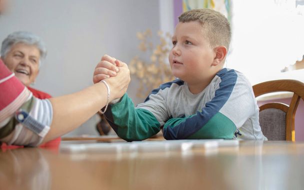 the boy shakes hands with his grandmother. he is very focused and serious. in the background is his great-grandmother, smiling and hoping that he will win - Фото, изображение
