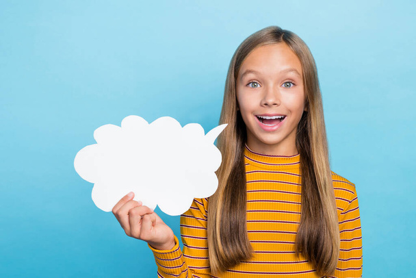 Portrait of cheerful positive school girl dressed yellow long sleeve hold white dialogue cloud talking isolated on blue color background. - Zdjęcie, obraz