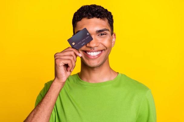 Closeup photo of young attractive smiling positive good mood nice guy cover face credit card vacation spend much money no problem isolated on yellow color background. - Фото, зображення