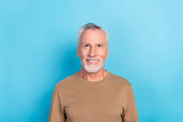 Photo of good mood optimistic senior man with gray hairstyle stubble wear beige t-shirt look empty space isolated on blue color background. - Foto, immagini