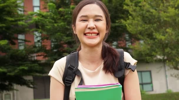 Красивая азиатка, готовящаяся к получению степени бакалавра в кампусе, держит книгу и счастливо улыбается. Образовательные концепции.  - Кадры, видео
