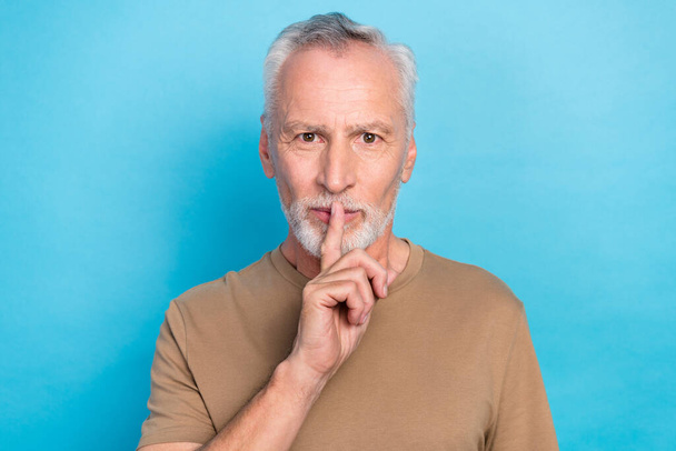 Photo of silent quiet positive man gray hairstyle stubble wear beige t-shirt hold finger on lips isolated on blue color background. - Foto, immagini