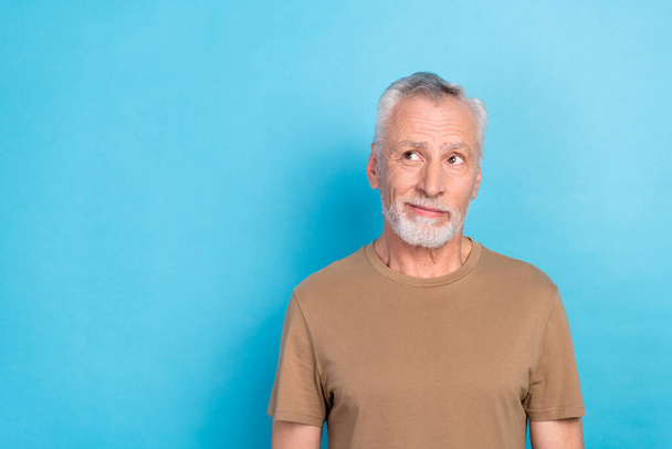 Photo of cheerful satisfied senior man with gray hairstyle stubble wear beige t-shirt look empty space isolated on blue color background. - Foto, Imagem