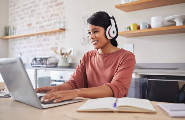 Email, music and black woman typing on the internet on a laptop while working at a table in her house. Remote African worker planning on web with technology while listening to a podcast in her home. - 写真・画像