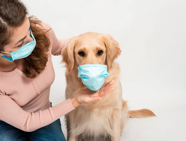 Vrouwelijke vrouw met medisch beschermd gezichtsmasker met hond Golden retriever op wit geïsoleerd. Een hond die naar een camera kijkt met medisch masker op een witte achtergrond. Dierenhygiëneconcept - Foto, afbeelding