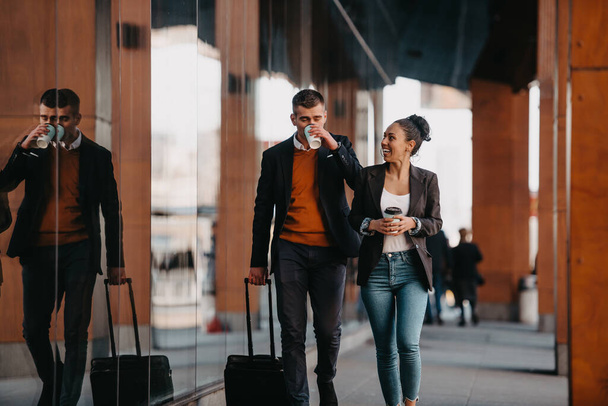 Business man and business woman talking and holding luggage traveling on a business trip, carrying fresh coffee in their hands.Business concept. High quality photo - Foto, Bild