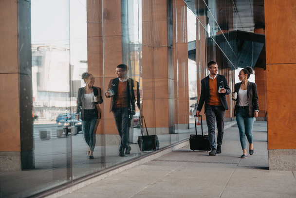 Business man and business woman talking and holding luggage traveling on a business trip, carrying fresh coffee in their hands.Business concept. High quality photo - Foto, Imagem