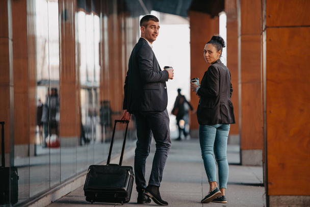 Business man and business woman talking and holding luggage traveling on a business trip, carrying fresh coffee in their hands.Business concept. High quality photo - Photo, image