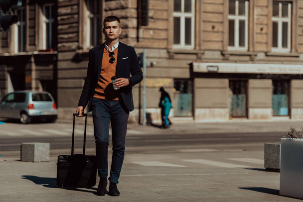 Going to airport terminal. Confident businessman traveler walking on city streets and pulling his suitcase drinking coffee and speaking on smartphone. High quality photo - Foto, Bild